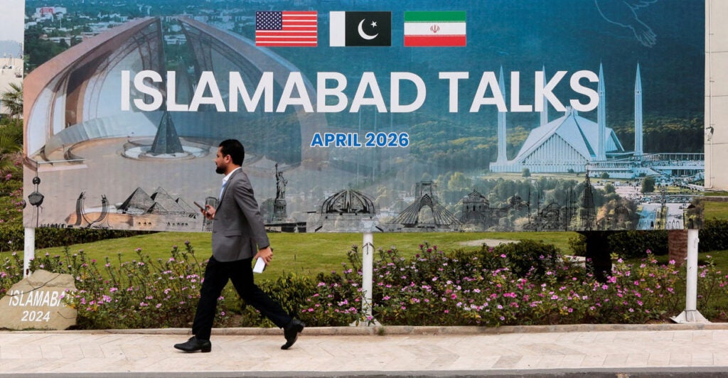 A man walks by a large sign reading "Islamabad Talks"