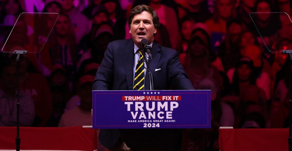 Tucker Carlson speaks from a Trump-Vance podium during 2024 campaign.