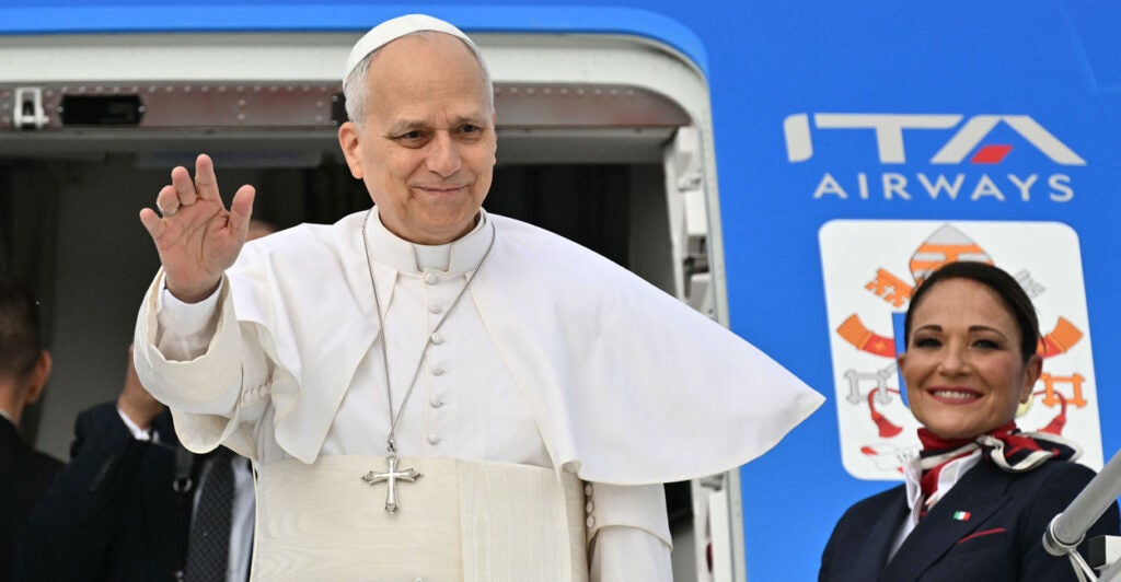 Pope Leo waves before boarding a plane, a female flight attendant at his side.