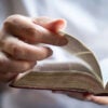 Close up of Bible in hands of young man in white shirt who is flipping the pages.