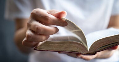 Close up of Bible in hands of young man in white shirt who is flipping the pages.