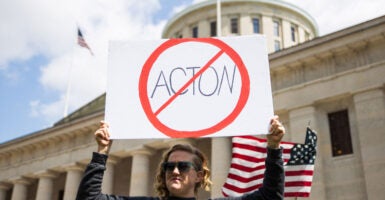 A woman stands outside of the Ohio capitol with a prohibition slash through symbol sign of 