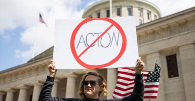 A woman stands outside of the Ohio capitol with a prohibition slash through symbol sign of 