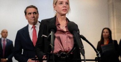 Pam Bondi in a purple blouse and black suit talks to reporters with Todd Blanche behind her.