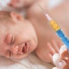 An Infant cries as a doctor holds a syringe up.