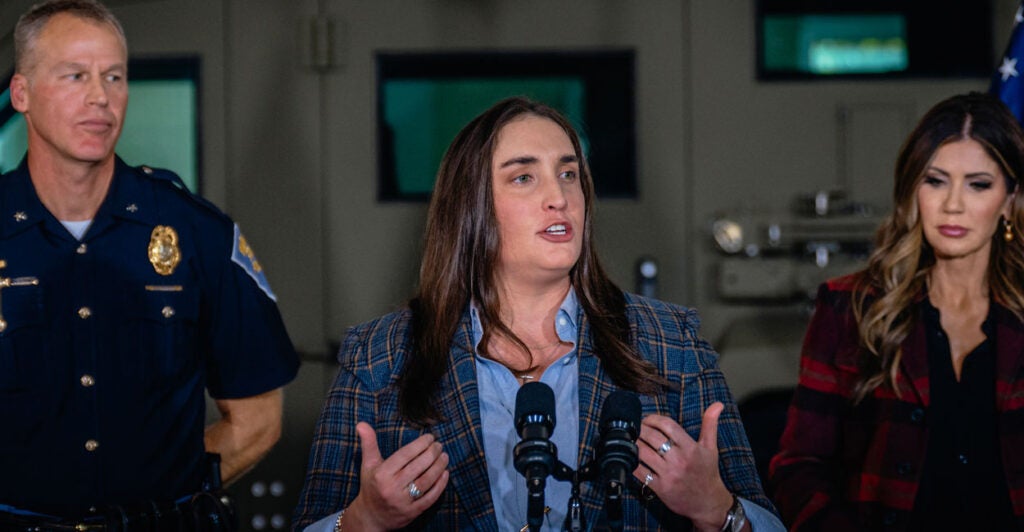 Former Immigration and Customs Enforcement Deputy Director Madison Sheahan stands in the center of a podium at a press conference.