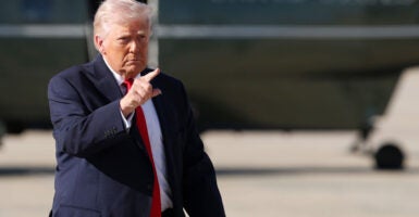 President Donald Trump points ahead of him with Air Force One in the background.