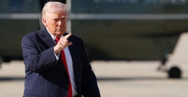President Donald Trump points ahead of him with Air Force One in the background.