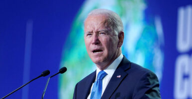 Joe Biden in a suit with a blue tie opens his mouth at a microphone