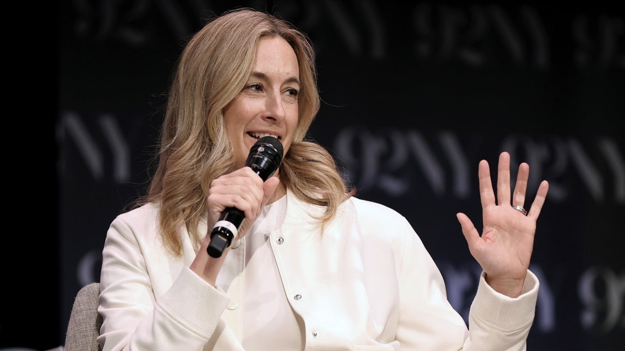 A woman with long blonde hair, wearing a white jacket, speaks into a microphone and gestures with her left hand on stage. The background features blurry 92NY text.